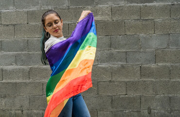 persona joven con la bandera del orgullo gay, joven mujer sobre fondo gris ondeando la bandera lgbtiq+ - obrazy, fototapety, plakaty