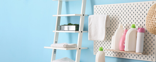 Pegboard with bottles of detergents and rack with towels near blue wall in laundry