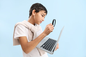 Little boy with magnifier and laptop on blue background