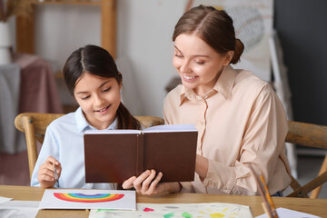 Drawing teacher with book giving private art lesson to little girl in workshop