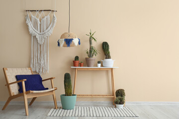 Interior of room with armchair, macrame and different cacti in pots near beige wall