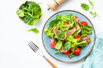 Green salad with fresh leaves, tomatoes and jamon at white table. Top view with copy space.