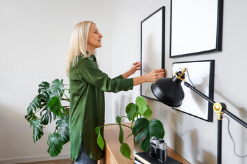 Mature woman hanging blank frame on light wall at home