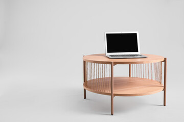 Wooden coffee table with modern laptop on grey background