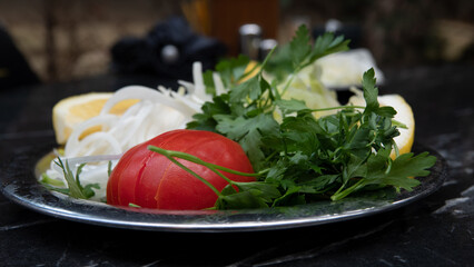Simple salad of sliced tomatoes, onions, lettuce and parsley served on plate on table. Begining antipasti before lahmacun service