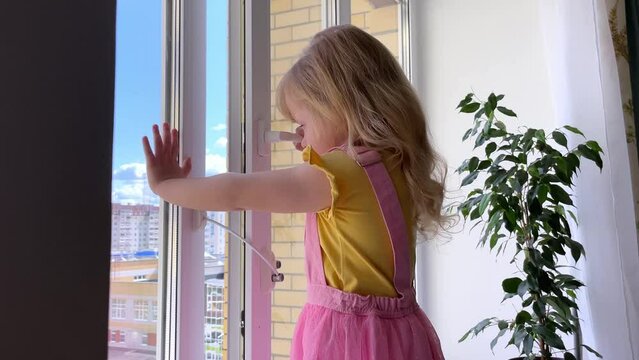 safety at home for small children. a lock on the window protects children from opening the window. The girl 4 years old tries to open the window standing on the windowsill on a high floor.