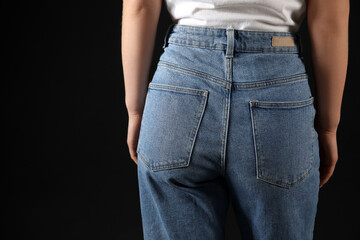 Young woman in stylish jeans on black background, back view