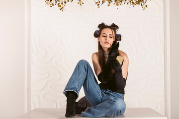 Obraz premium Portrait of A beautiful girl in a corset and elbow length gloves with hair in curlers is doing her makeup, applying lipstick. getting ready for an elegant evening meeting or party.