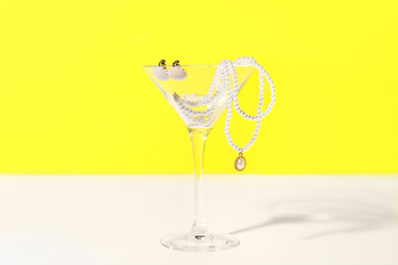 Glass with pearl jewelry on table against yellow background