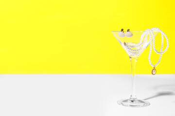 Glass with pearl jewelry on table against yellow background