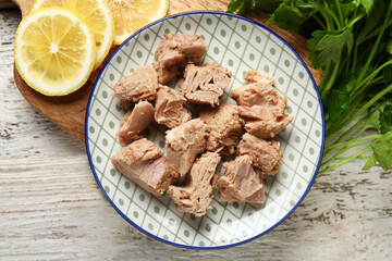Plate with delicious canned tuna, lemons and parsley on white wooden table