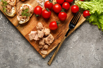 Board with delicious canned tuna, tomatoes and lettuce on grey grunge table