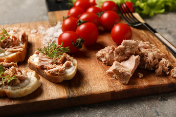 Board with delicious canned tuna, tomatoes and bruschettas on grey grunge table, closeup