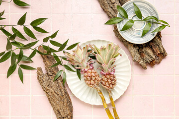 Plates with decorative pineapples, plant branches and tree barks on pink tile background