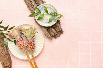 Plates with decorative pineapples, plant branches and tree barks on pink tile background