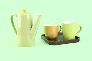 Teapot and tray with mugs on green background