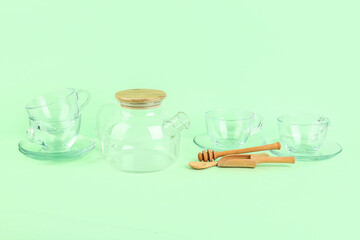 Teapot, cups, honey dipper and scoop on green background