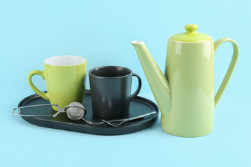 Teapot and tray with mugs on blue background