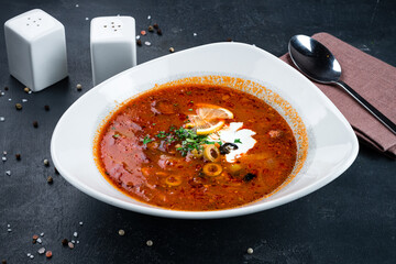 Solyanka soup with ham, meat, olives, tomatoes, sour cream, lemon and greens.