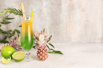 Glass of cocktail with mini pineapples and lime on table near grunge wall