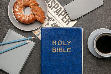 Holy Bible with notebook, mobile phone, cake, coffee cup and newspaper on dark background