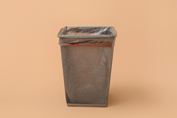 Empty trash bin with garbage bag on beige background