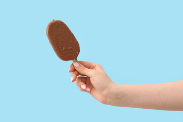 Woman holding delicious chocolate covered ice cream on stick against blue background