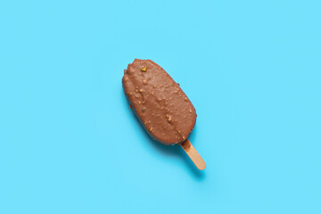 Delicious chocolate covered ice cream on stick against blue background