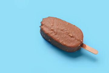Delicious chocolate covered ice cream on stick against blue background