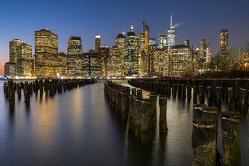 Fototapeta na wymiar View of lower Manhattan at dusk seen from Brooklyn. Remaining of an old pier can be seen at the foreground and city skyline in the background