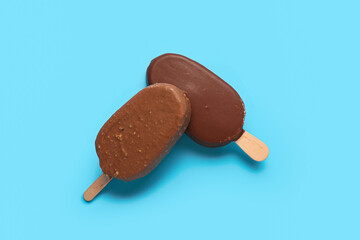 Delicious chocolate covered ice cream on stick against blue background