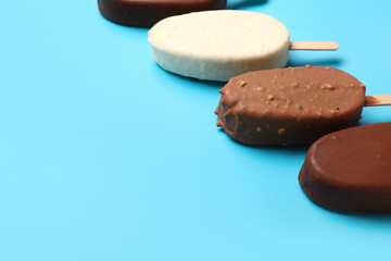 Composition with different chocolate covered ice cream on stick against blue background
