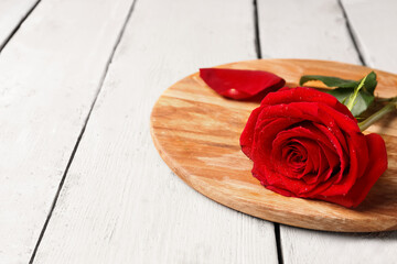 Board with beautiful red rose and petal on light wooden background