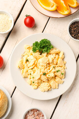 Composition with plate of delicious scrambled eggs with ingredients on white wooden background