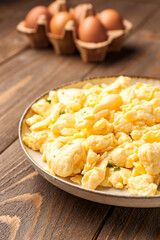 Plate of scrambled eggs on brown wooden background
