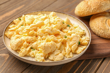 Plate of scrambled eggs and fresh buns on brown wooden background