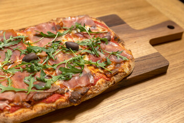 Arugula prosciutto pizza served on a wooden board