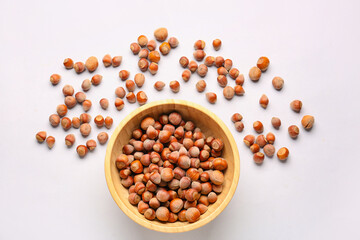 Bowl with shelled hazelnuts on light background