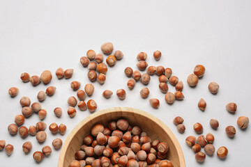 Bowl with shelled hazelnuts on light background