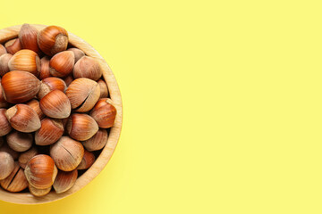Bowl with shelled hazelnuts on yellow background