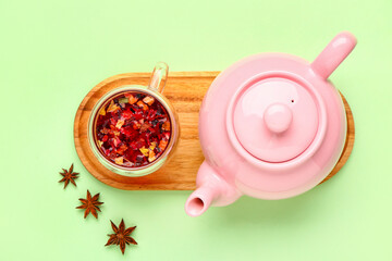 Board with teapot and cup of fruit tea on green background