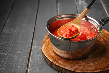 Saucepan and spoon with tasty tomato sauce on dark wooden background