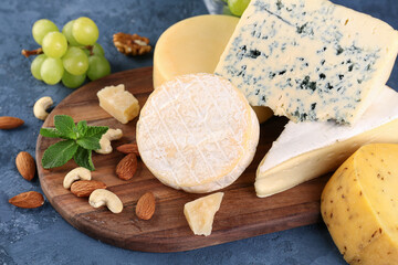 Wooden board with different types of cheese on blue background