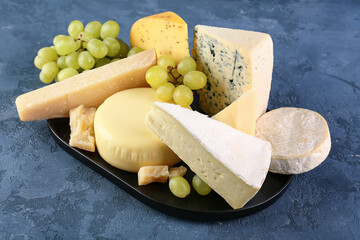 Plate with different types of cheese on blue background