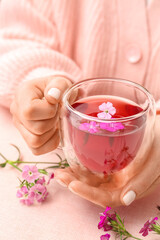Fototapeta na wymiar Female hands with cup of tea and delicate flowers on pink table