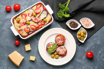 Plate and baking dish of tasty Eggplant Parmesan with ingredients on blue background