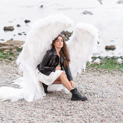 beautiful young woman with white wings. White angel in leather jacket and in white silk dress. holy woman 