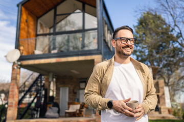 Happy Homeowner Man with Cup of Tea Stand in Front of Modern House