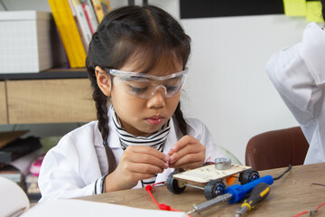 School student making robotic cars. Girl at robotics school makes robot managed from the constructor, child learns robot constructing.