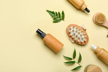 Bottles of cosmetic oil with plant twigs and massage brushes on beige background